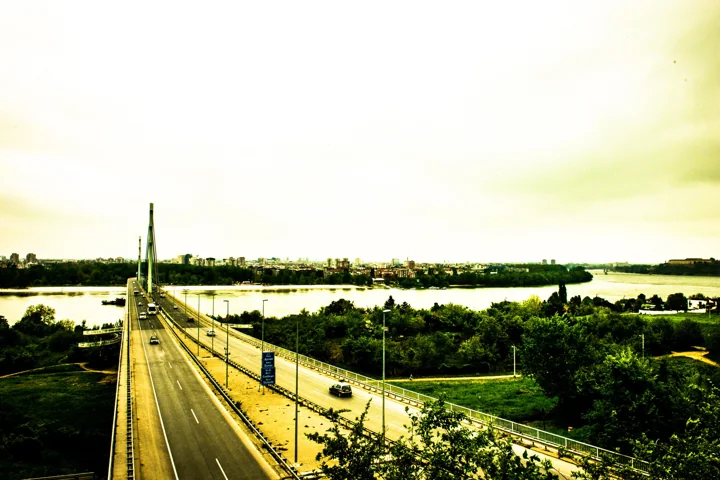 A road bridge crossing the river between green banks beneath a bright sky