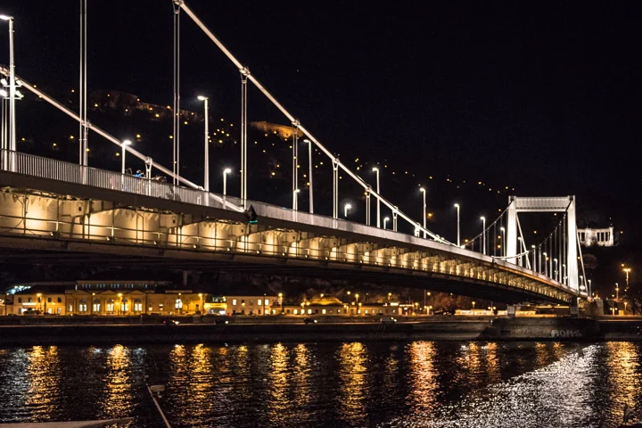 A brightly lit suspension bridge reflected in dark water