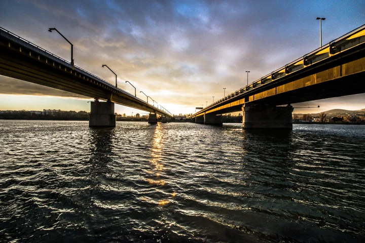 Two parallel bridges viewed from the water beneath a cloudy evening sky